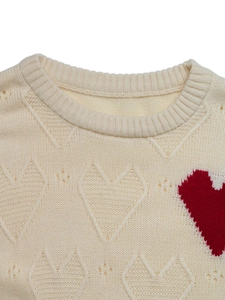 Detail of crew neck sweater with textured heart knit patterns and a red contrast heart