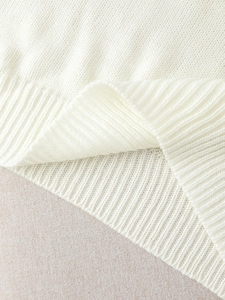 Detailed close-up of soft white knit sweater featuring ribbed hem and fine stitch texture