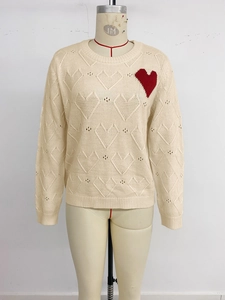 Detail of heart-shaped hollow knit pattern and red heart patch on cream crewneck sweater