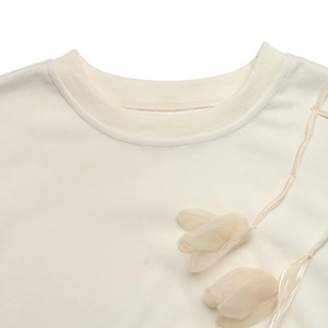Detailed macro view of cream-colored knit top with 3D floral and ribbon shoulder detail