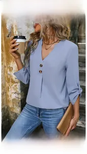 Detail of light blue V-neck blouse featuring amber buttons and adjustable roll-up sleeves