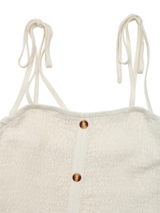 Detail of cream smocked camisole top featuring adjustable tie straps and tortoise buttons