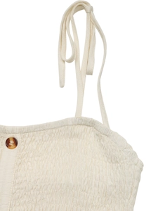 Detail of off-white shirred fabric with spaghetti straps and amber buttons on the dress