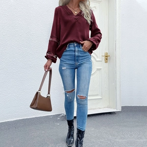 Detail of burgundy V-neck blouse featuring intricate lace trim and hollow sleeve patchwork