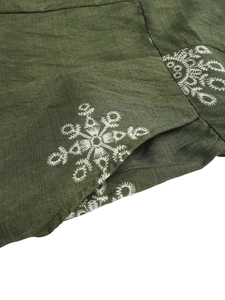 Detail of white snowflake embroidery on dark green linen fabric with rich texture
