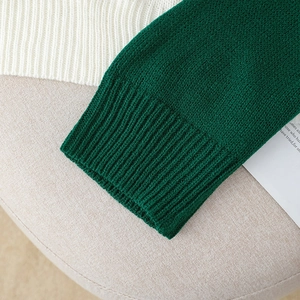 Close-up of loose knit sweater featuring dark green ribbed cuffs and cream knit texture
