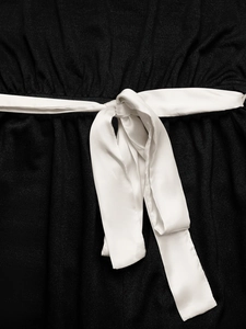 Détail du nœud en satin blanc contrasté sur une combinaison noire en coton et lin texturé