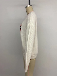 Close-up of white chunky knit sweater featuring a red heart embroidery on the side