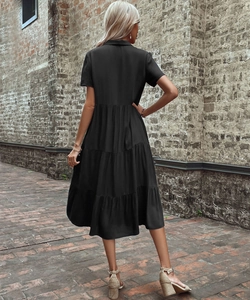 Back view of a black short-sleeved tiered midi dress with a collar on a brick path