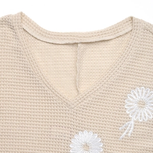 Détail du tissu gaufré beige avec broderie marguerite blanche et col en V sur le haut