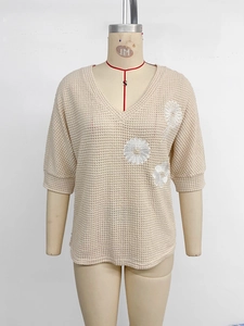 Détail du haut en maille gaufrée beige avec col en V et broderies de marguerites blanches fines