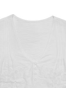 Detail of white V-neck shirt showing floral embroidery, buttons, and textured fabric