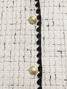 Close-up of white tweed texture with black crochet lace and gold dome buttons