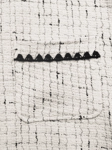 Detailed macro of white tweed fabric with black woven trim on the pocket of a cardigan