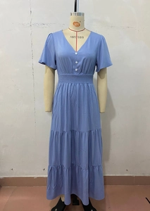 Dettaglio dell'abito blu con scollo a V, balze a strati e bottoni bianchi decorativi