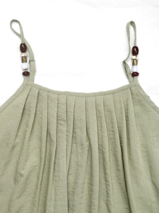 Detail of green linen dress featuring ethnic beads on straps and pleated texture