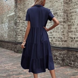 Short sleeve dark blue lapel tiered midi dress displayed against a vintage red brick wall