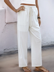 Detail shot of white high-waisted linen trousers featuring drawstring waist and front pockets
