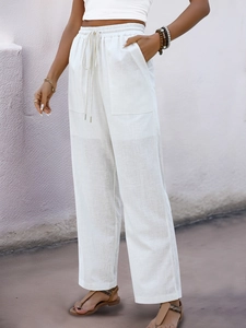 Detail of high-waisted white linen pants featuring elastic drawstring and large patch pockets