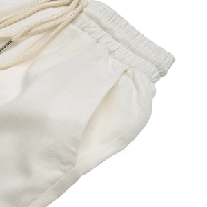 Detail of white high-waisted linen trousers featuring elastic waistband and cotton drawstring