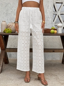 Detail of white crochet lace pants with high waist drawstring and bohemian floral patterns