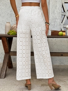 Detail of high-waisted white lace trousers featuring geometric hollow-out patterns