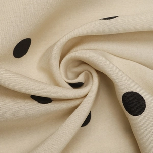 Primo piano del tessuto twill beige a pois neri che mostra la trama e il drappeggio
