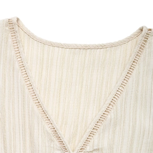 Détail du col en V avec broderie échelle sur un tissu beige à texture gaufrée