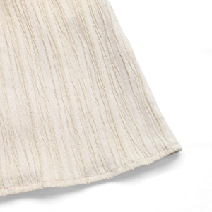 Vue macro du tissu beige d'une robe d'été montrant la texture plissée et l'ourlet
