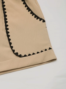 Detail of beige linen shorts featuring black scalloped crochet trim on the pocket edge