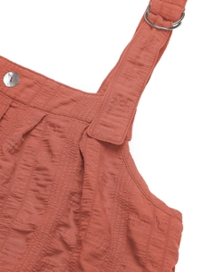Detail of rust red seersucker fabric with metal adjustment buckle and pearl button