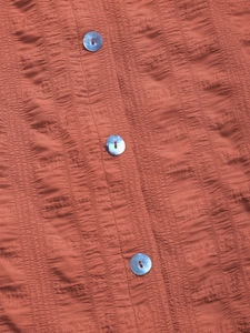 Macro shot of rust red plissé fabric with iridescent blue buttons on a sundress