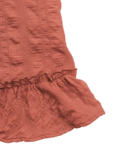Detail of terracotta smocked dress featuring textured fabric and delicate ruffle hem