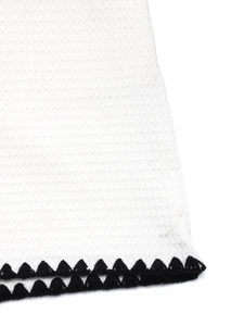 Detail of white waffle texture shorts with black crochet triangle trim at the hemline
