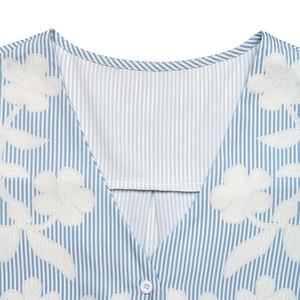 Detail showing white floral embroidery on blue and white striped V-neck cotton shirt