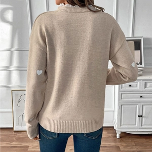 Detail of beige knit sweater featuring white heart patches on elbows and lace collar accent