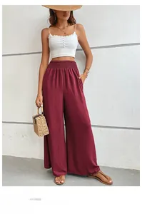 Detail of high-waisted smocked waistband and pleated fabric on burgundy wide-leg trousers