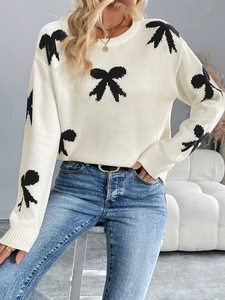 Close-up of elegant white knit sweater featuring black bow jacquard patterns and round neck