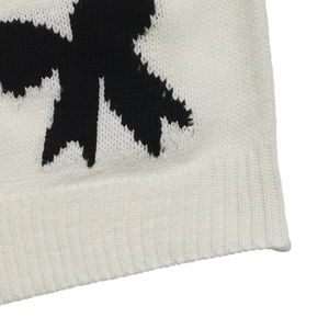 Detail of cream knit sweater showing black bow jacquard pattern and ribbed cuff finish