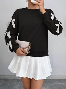 Detail of long sleeve black sweatshirt with white ribbon bows and pleated skirt