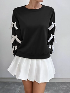 Detail of black long-sleeve sweatshirt featuring white bow accents on sleeves and pleated skirt