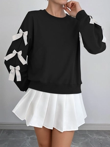 Detail of black sweatshirt sleeves featuring white decorative bows and ribbed cuffs