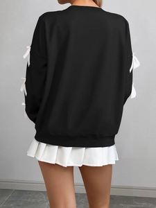 Detail view of long sleeve sweatshirt featuring white 3D bow accents on black sleeves