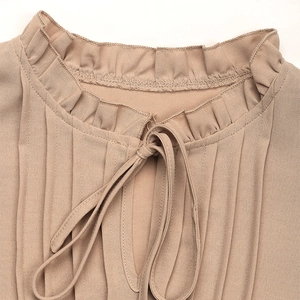 Detalle de cuello con volantes, lazo ajustable y textura de tela plisada elegante de mujer