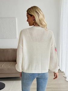Detail view of white openwork knit cardigan with red strawberry floral embroidery on sleeves