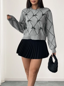 Detail of grey diamond pattern sweater with small black bows and black pleated skirt