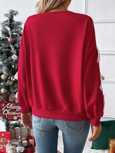 Detail view of red pullover sweatshirt with white bow accents on sleeves in Christmas setting