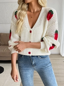 Close-up of white chunky knit cardigan featuring strawberry embroidery and red buttons