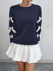 Close-up of navy blue sweatshirt featuring decorative white bows on sleeves and pleated skirt