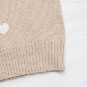 Close-up of heart print pattern on beige knit sweater with ribbed hem detail
